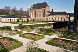 Clipped Buxus sempervirens (Common Boxwood) hedges edging square garden beds on gravel paths, with cone topiary and a brick castle beside a moat.