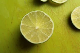 Citrus lime 'Sublime' (Key Lime) fruit halved to show pale green segments and thin green rind, on a scratched green chopping board.