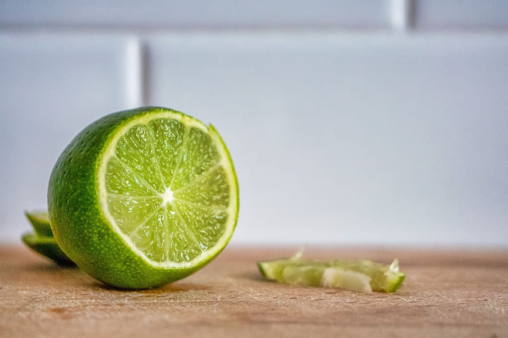 Halved Citrus lime 'Sublime' (Key Lime) fruit with bright green skin and juicy segments, sitting cut side out on a wooden board.