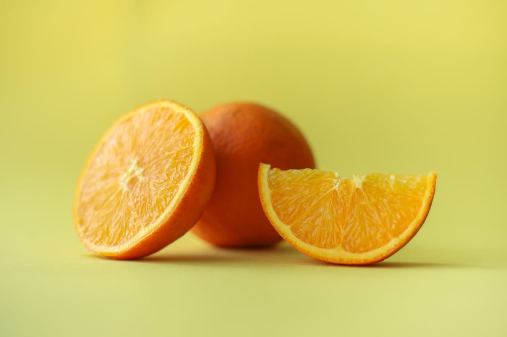 Citrus orange 'Carter's Navel' (orange): a halved fruit, a whole fruit and a juicy wedge with bright orange flesh against a soft yellow-green background.