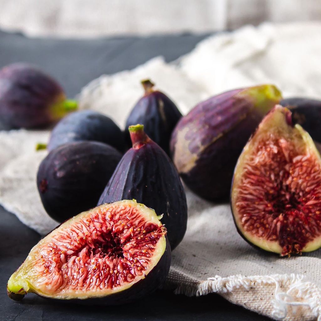 Ficus carica 'Brunoro Black' fig fruit, whole and halved, with purple-black skin and red seeded flesh, resting on pale linen.