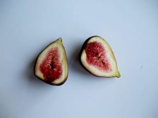 Ficus carica 'French Sugar' fig halved to show a red seeded centre, pale rind and dark purple skin, on a plain pale background.