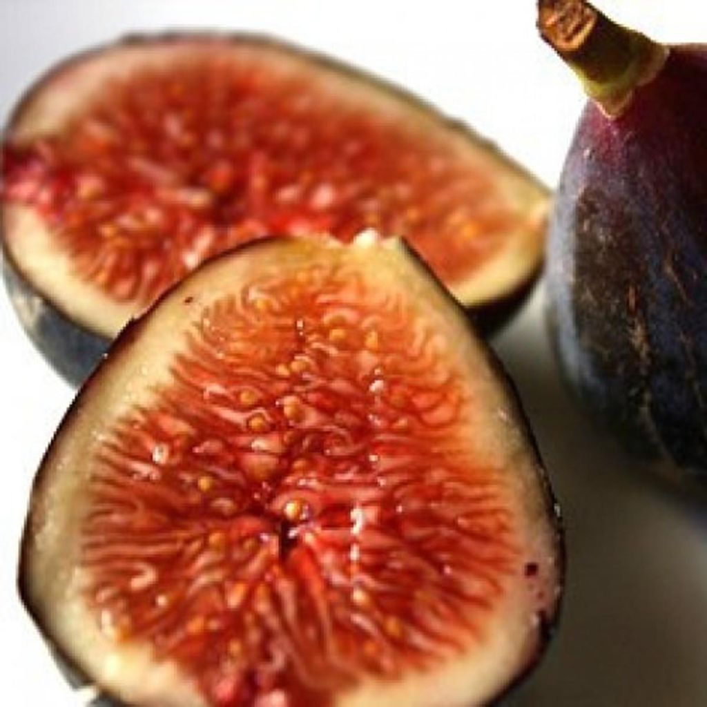 Fig 'Mrs Williams' (Ficus carica) fruit, two halves cut open to show red-orange flesh and seeds, beside a whole dark purple fig with its stalk.
