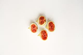 Four halved Ficus carica 'Ventura' figs on a white background, showing green skin and red-orange inner flesh with small seeds.