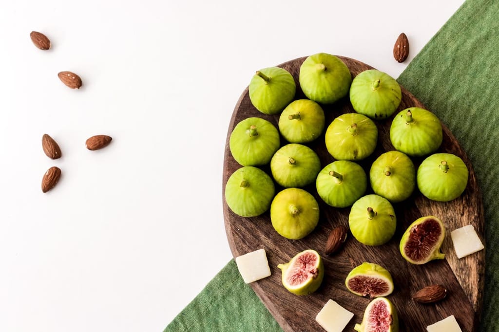 Ficus carica 'Ventura' fig fruit, green-skinned whole and halved figs showing pink-red flesh, on a wooden board with almonds and cheese.