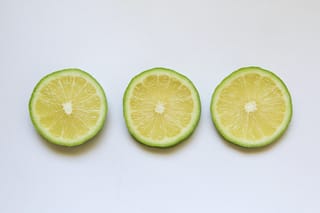 Three cross-section slices of Citrus lime 'Bearss' (Persian Lime) in a row, showing pale yellow-green flesh and thin green rind on white.