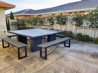 Michelia 'Fairy Cream' (Fairy Magnolia) trained along a wooden fence, with cream flowers, beside a paved patio with a large outdoor table and benches.