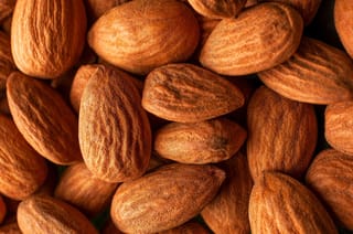 Close-up of shelled Almond 'Monovale' (Prunus dulcis) kernels, piled together, with brown skins showing fine ridges and a warm reddish tone.
