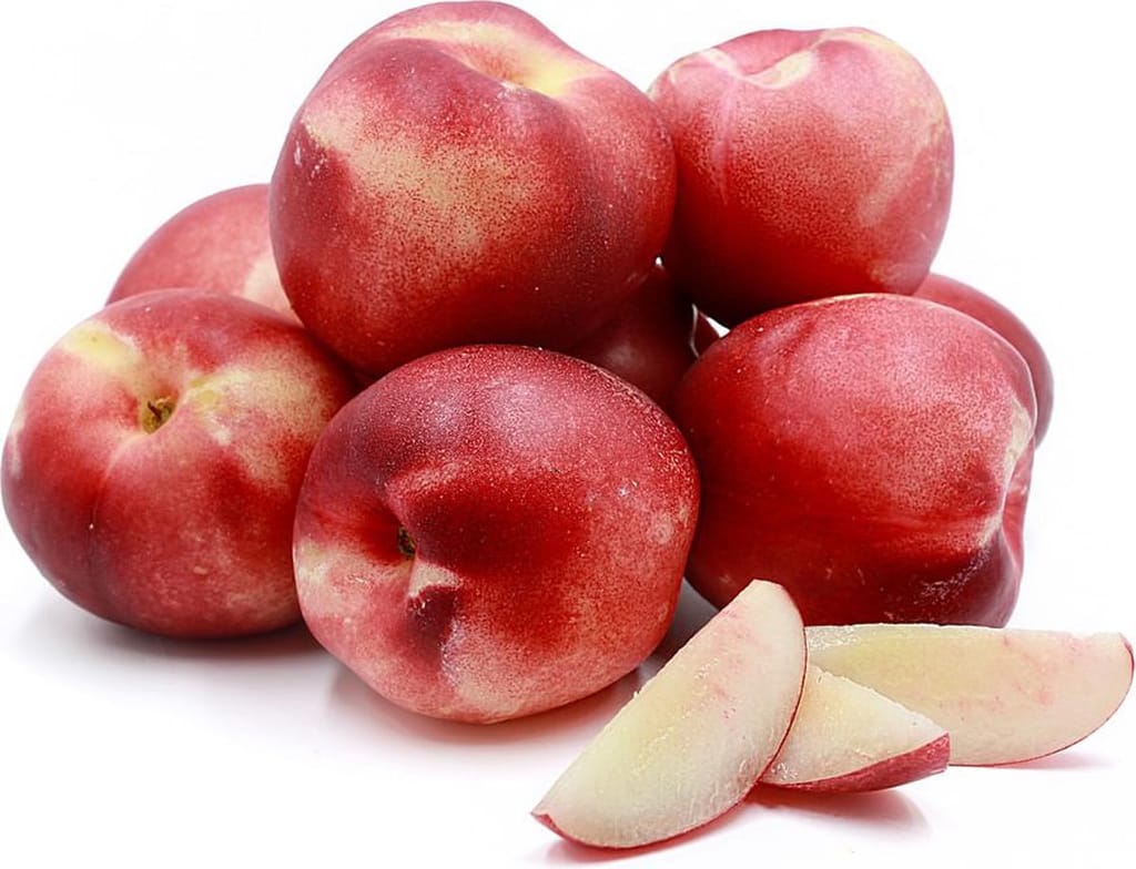 Nectarine 'Snow Queen' fruit, a pile of red-blushed nectarines with yellow-cream patches, beside three pale white-fleshed slices on white.
