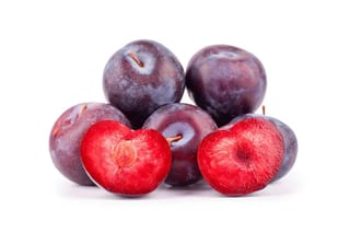 Plum 'Billington' (Japanese plum) fruit with dark purple skin, two halves showing bright red flesh, piled against a white background.
