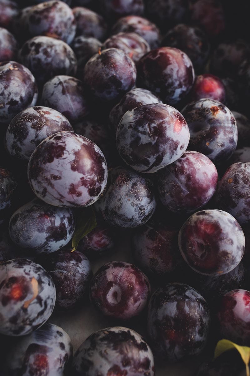 Plum 'Black Doris/Billington' (Japanese Plum) fruit, a pile of ripe dark purple plums with a dusty blue bloom and red patches.