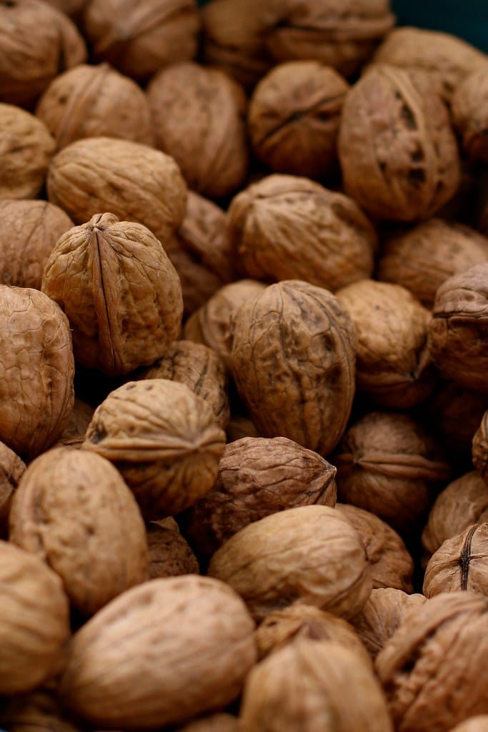 Walnut 'Shannon' (English Walnut) nuts in their light brown wrinkled shells, piled closely together and filling the frame.