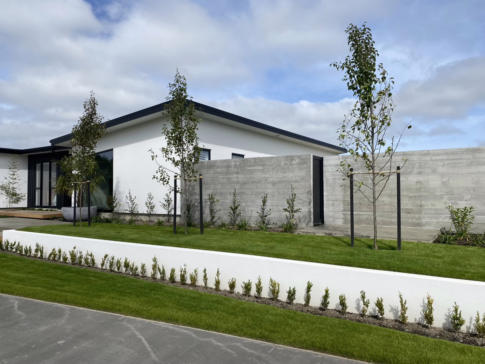 Modern home featuring Pyrus calleryana 'Slim Jim' trees in the front yard. The landscape includes a white retaining wall, concrete wall, and lush green lawn.