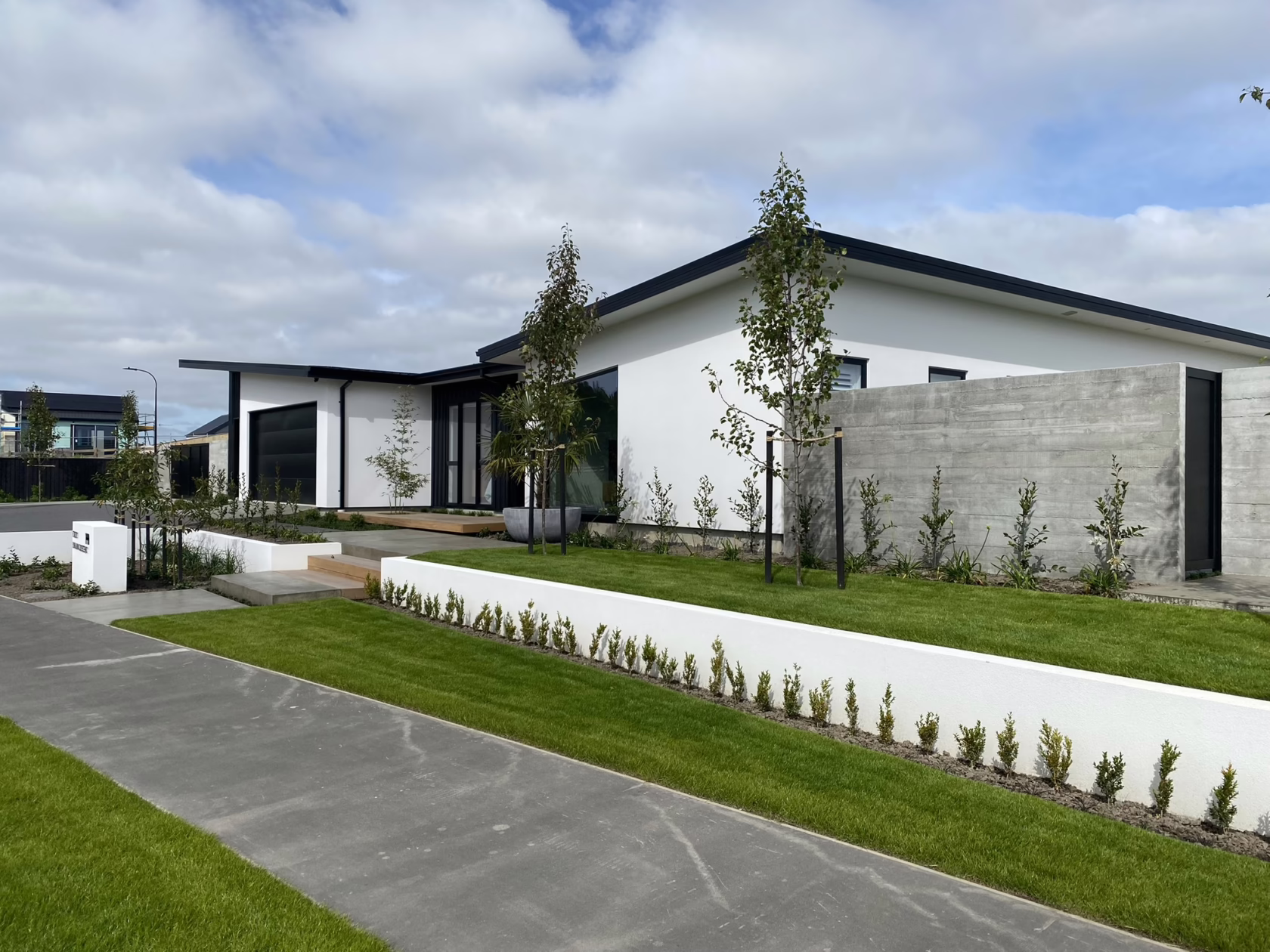 Modern white house with Pyrus calleryana 'Slim Jim' trees lining the manicured lawn and concrete wall. Featured by Epic Landscape Design, the scene showcases clean lines and contemporary landscape architecture.