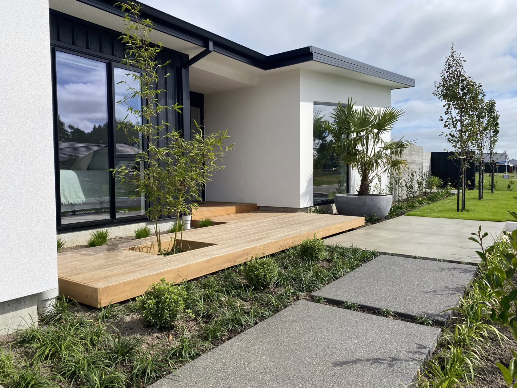 Modern home exterior featuring Pyrus calleryana ‘Slim Jim’ trees lining the lawn, complemented by a wooden deck and minimalist landscaping. The home has a sleek, black-and-white design with large windows.