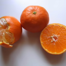 Bright orange Tangelo 'Seminole' citrus fruit. One whole, one peeled, and one sliced in half showing juicy segments.