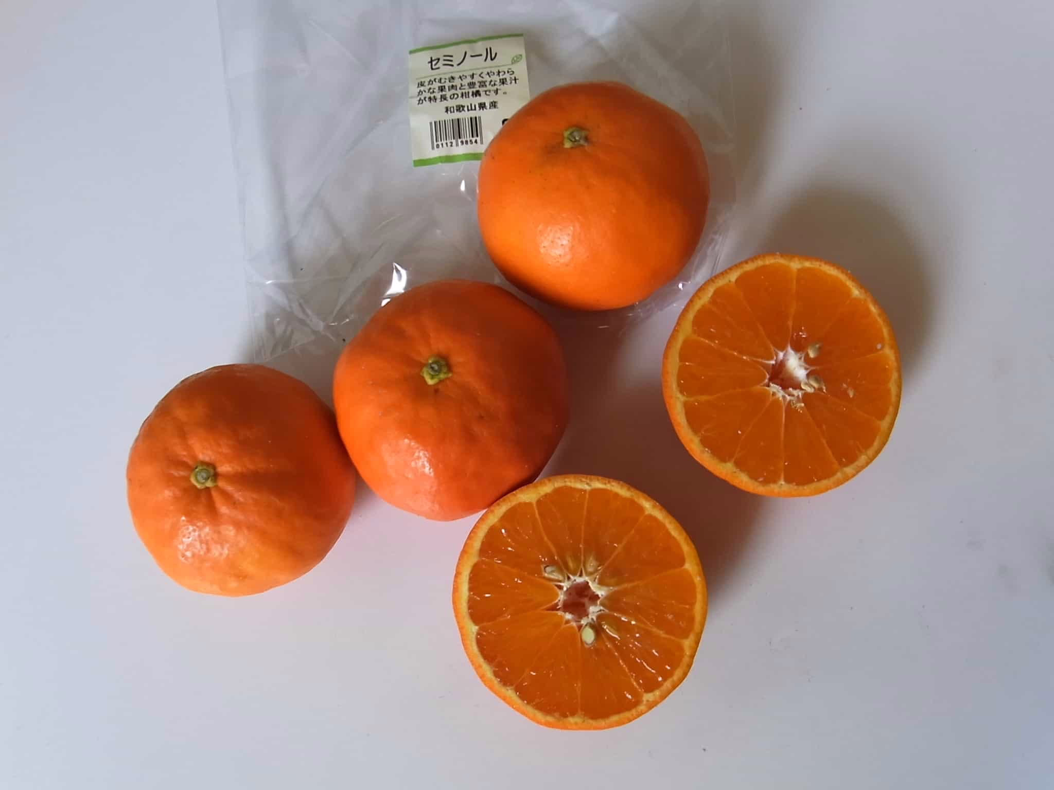 Fresh Tangelo 'Seminole' citrus fruit: Three whole and two halves display the vibrant orange color and juicy segments, with Japanese labeling.