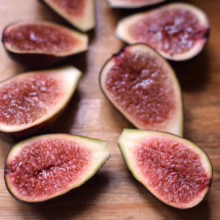 Close-up of ripe figs, sliced in half to reveal their vibrant red interior and tiny seeds, resting on a warm wooden surface. The figs showcase a fresh and healthy snack.