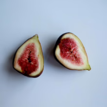 Two fig halves showcase their vibrant red pulp and creamy white flesh against a plain background, highlighting the fruit's texture and color.