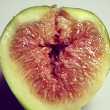 Cross-section of a ripe green fig, revealing its juicy, pinkish-red interior filled with tiny seeds.