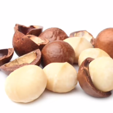 Pile of shelled and unshelled macadamia nuts on a white background. Some nuts are whole, others are halved, showcasing their creamy color and texture.