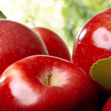 Close-up of several shiny, bright red apples with green leaves, showcasing their vibrant color and fresh appearance.