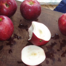 Fresh, shiny red apples on a wooden cutting board, one apple sliced with a bite taken. A healthy snack or ingredient for baking.