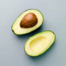 Halved avocado on a light blue surface. One half contains the brown pit, the other is empty, showcasing the creamy green flesh. Fresh, healthy eating.
