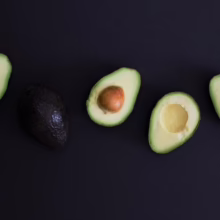 Arrangement of avocado halves and a whole avocado on a dark background. Ripe avocados, healthy eating, food photography.