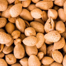 Pile of whole almonds in their shells. The almonds are a light brown color and have a textured surface.