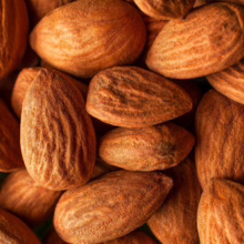 Close-up of a pile of brown almonds. The nuts have detailed ridges and a textured surface, creating a warm, natural food scene.