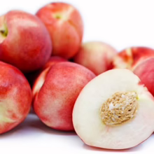 Pile of fresh, ripe white nectarines, one cut in half to reveal the pit. The fruit has a smooth red and white skin.
