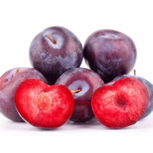 A cluster of ripe plums, some whole with a deep purple skin speckled with lighter dots, and two halved plums revealing a juicy red interior and smooth pit.